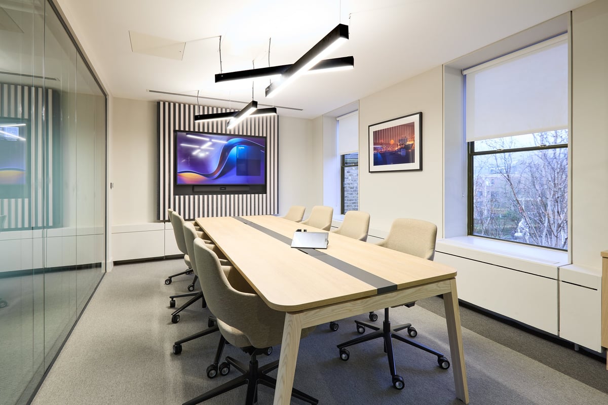 Modern conference room with white table, beige chairs, wall-mounted TV, and large windows with winter landscape view