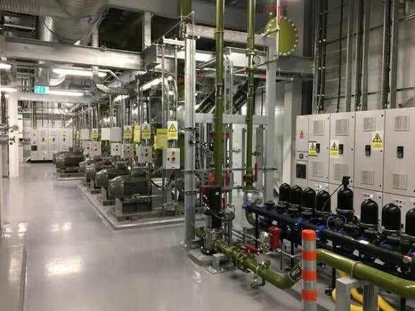 Industrial facility interior with large machinery, piping systems, electrical control panels, and industrial equipment in a warehouse setting